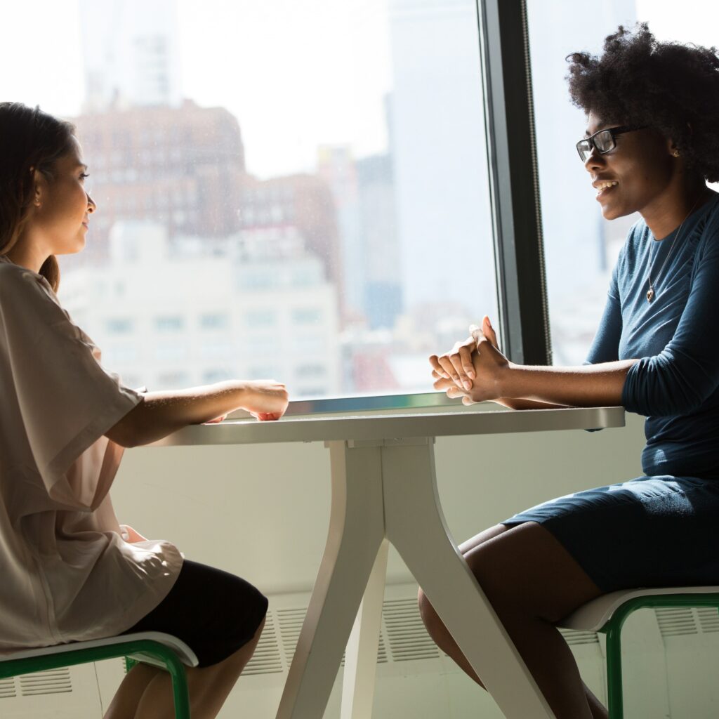 Dos mujeres sentadas teniendo una conversación, representando a dos personas hablando sobre cómo hacer crecer nuevas empresas. 